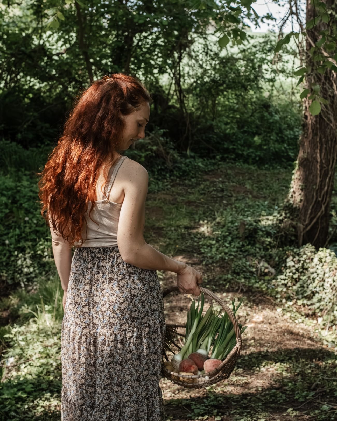 Laura Bridier de dos dans un sous-bois, un panier de légumes à la main.
