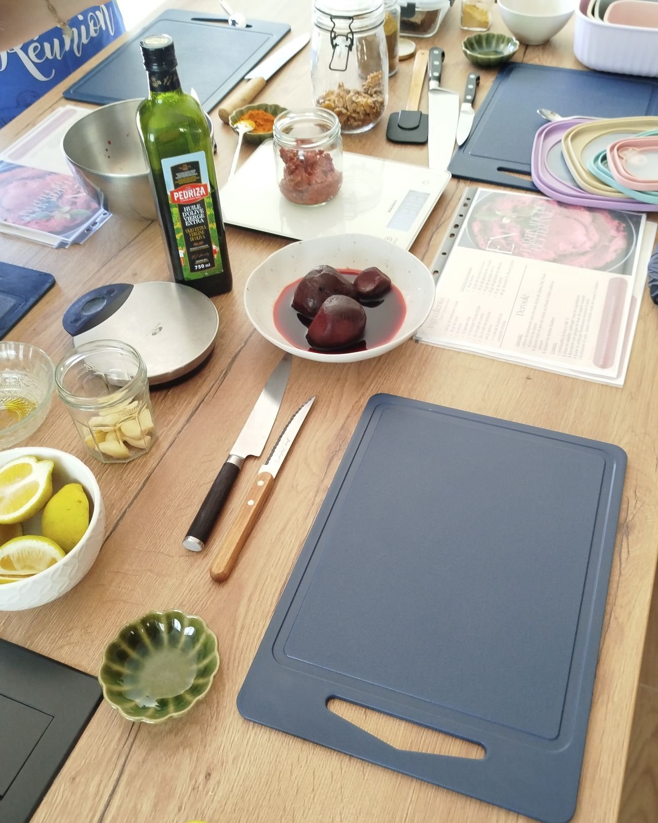 Plan de travail préparé pour un atelier : planches à découper, huile d'olive, citrons et fiches recettes.