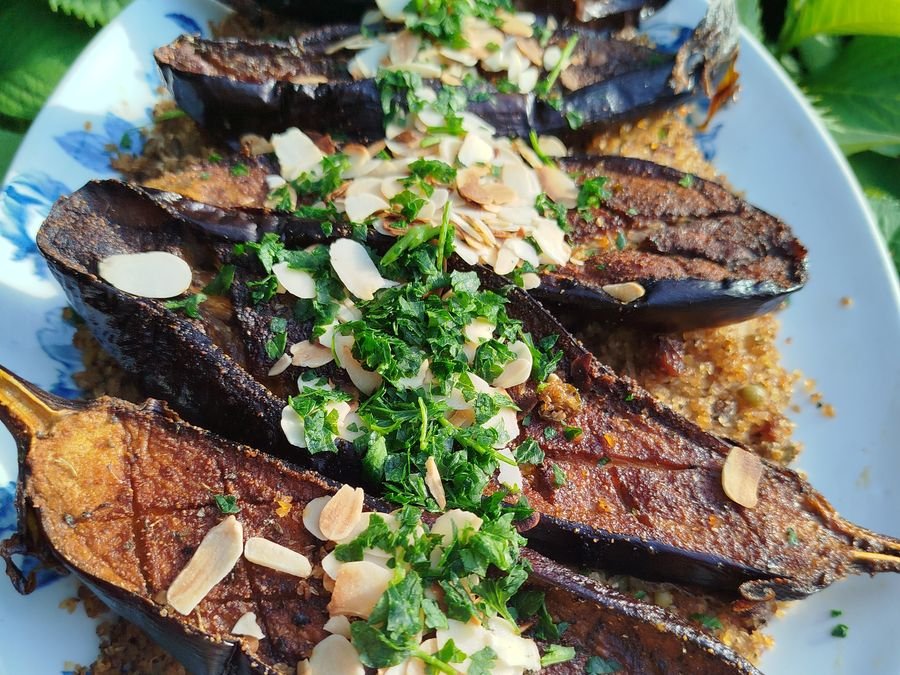 Aubergines rôties entières, parsemées d'amandes effilées et d'herbes fraîches.